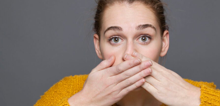 negative feelings concept - dumbstruck beautiful 20s girl covering her mouth for regret or mistake,studio shot on gray background