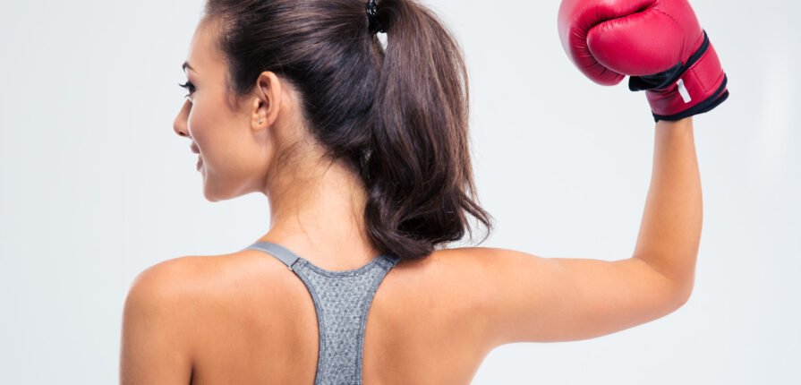 Back view portrait of a sports woman standing with boxing gloves in victory pose isolated on a white background